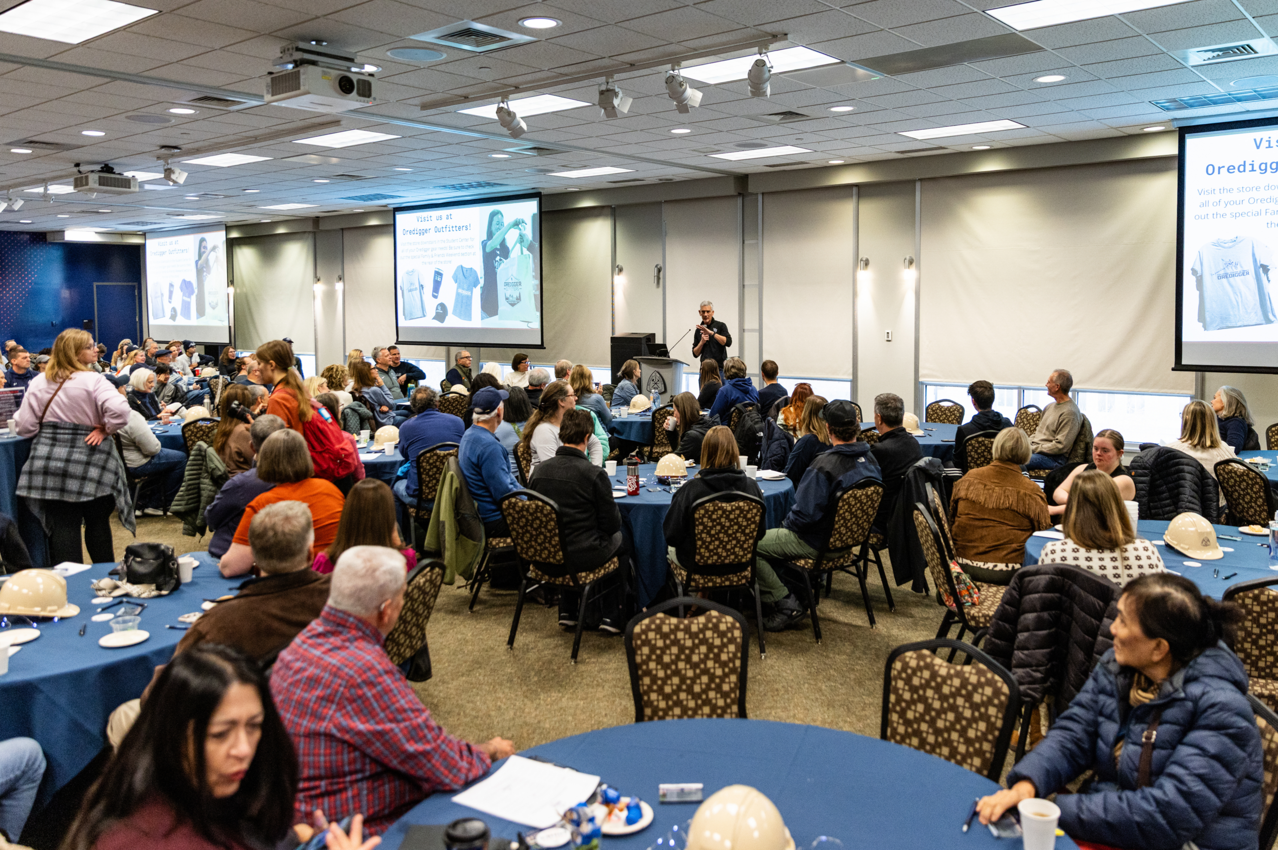 families and students sit around round tables while listening to the welcome from President Paul C. Johnson